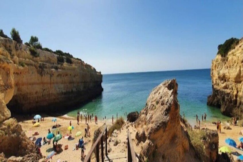 A coastal beach with clear waters, rocky cliffs, and people sunbathing. 2