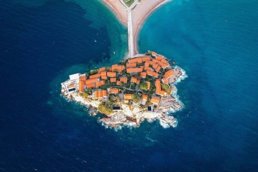 An aerial view of a coastal island with red-roofed buildings and a beach. 5