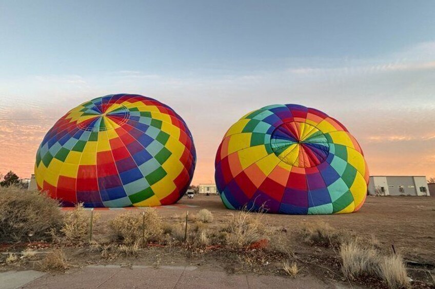 Two large, colorful hot air balloons parked on a field with buildings in the background. 3