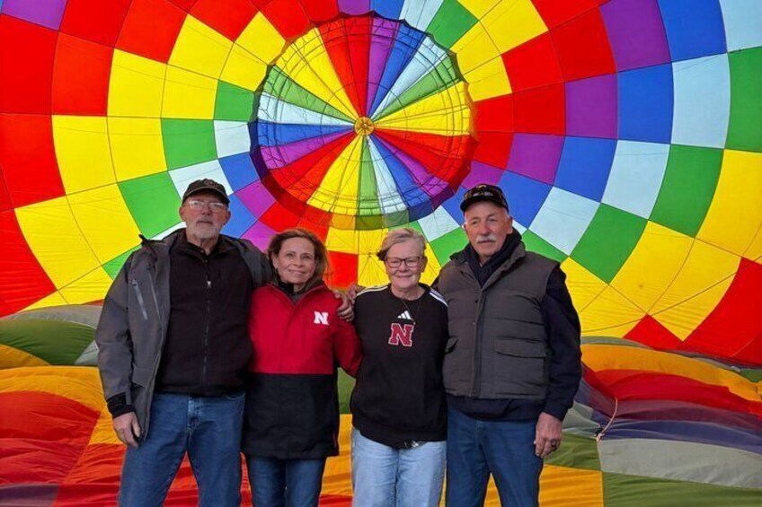 Four people standing in front of a colorful hot air balloon. 5