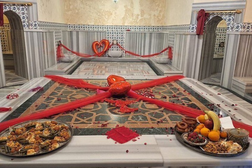 A decorated dining table with a red cloth, a heart-shaped decoration, and various food items. 3
