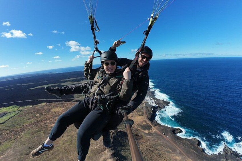Two people paragliding over a coastal landscape with ocean waves below. 2