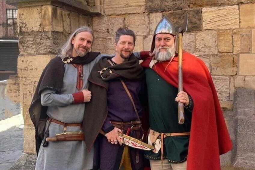 Three people dressed in medieval costumes standing in front of a stone wall. 1