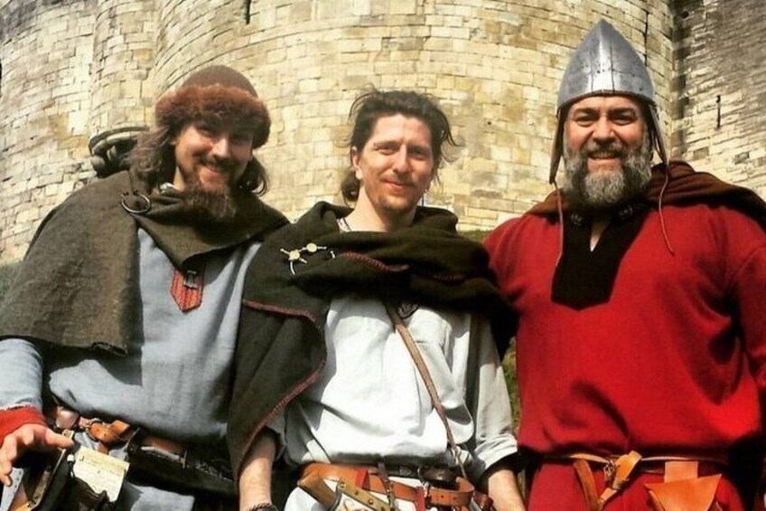 Three people in historical costumes standing in front of a stone wall. 3