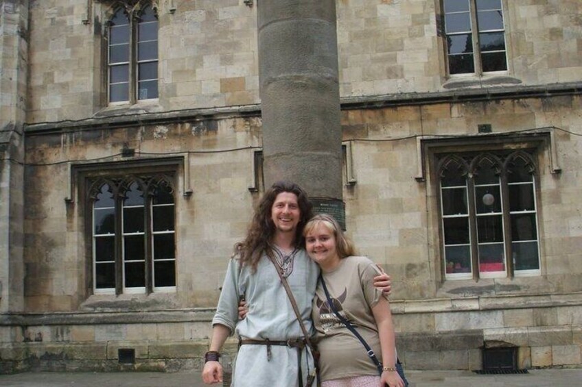 Two people standing in front of a historic building with arched windows and a large stone column. 4