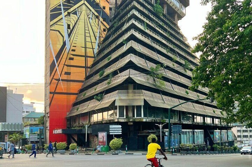 A modern building with a unique angular design, surrounded by pedestrians and greenery. 2
