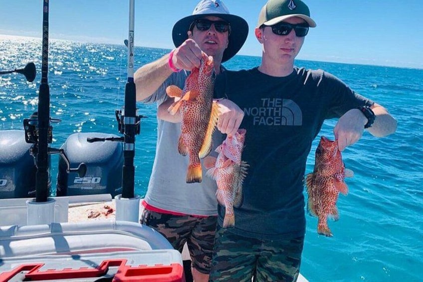 Two people holding fish on a boat with fishing rods and a water motor. 3