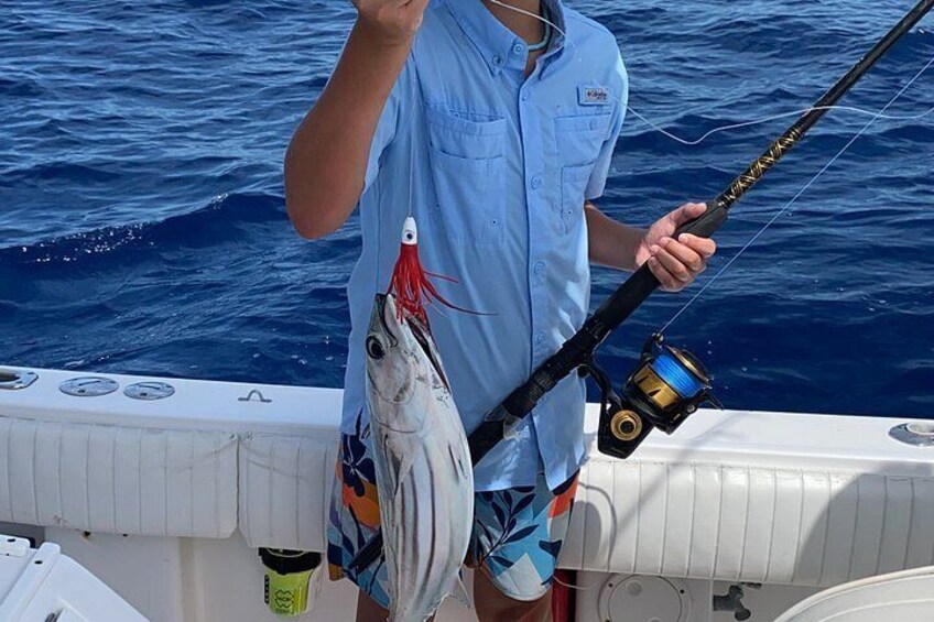 A person holding a fishing rod with a fish on it, standing on a boat in the water. 2