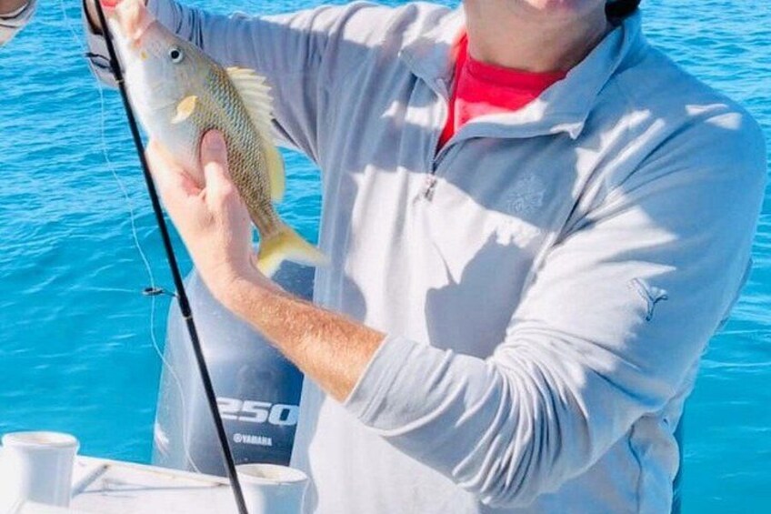 A person holding a fish, wearing a white jacket, and standing by a body of water. 5