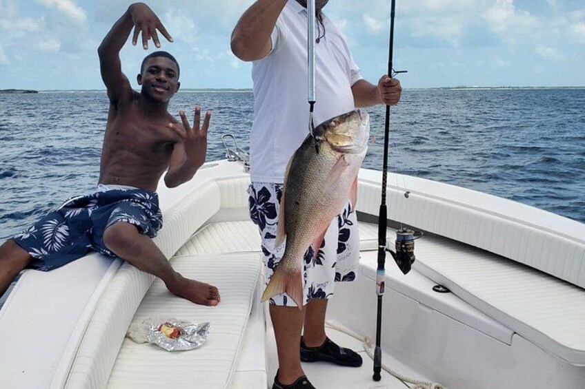 Two people on a boat holding a fish, with water and sky in the background. 4