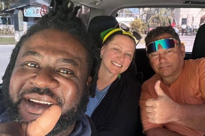 Three people in a car with a city street in the background. 3