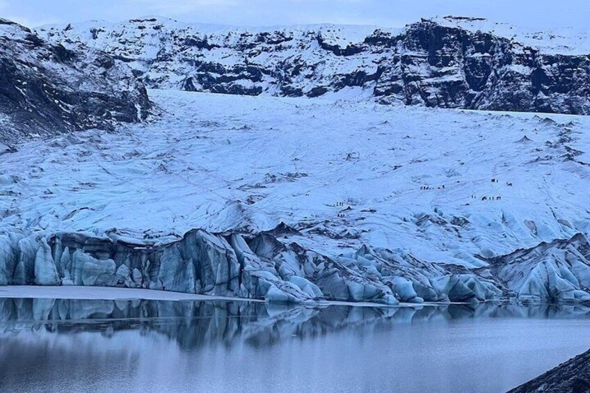 A glacier with a calm lake reflecting its surface, surrounded by snow-covered mountains. 5