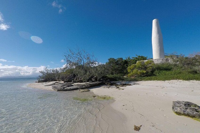 A sandy beach with clear water, a large white monument, and sparse vegetation. 4