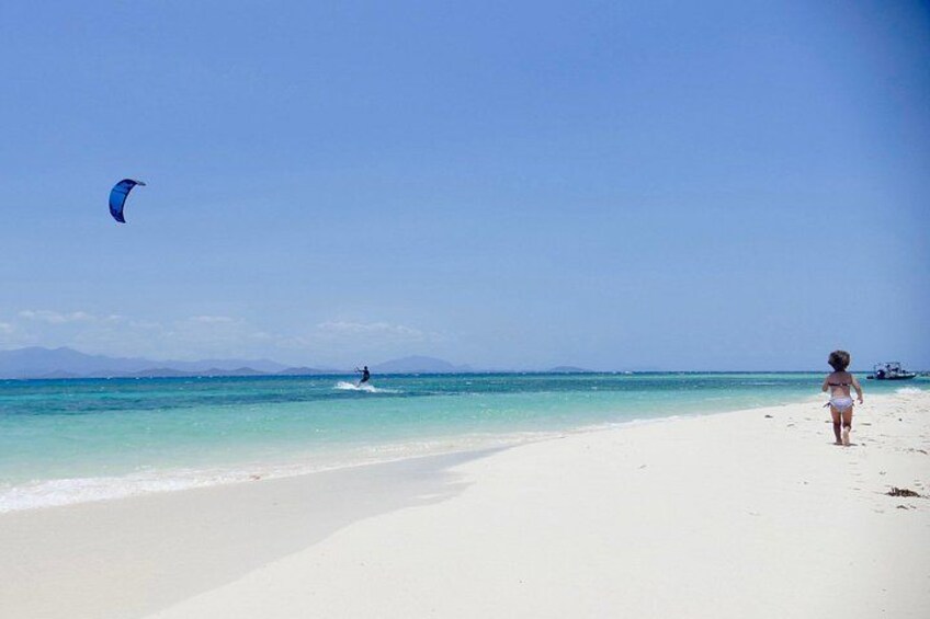 A beach with a person walking and a kite surfer in the water. 2