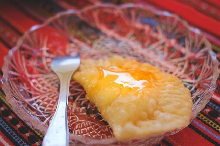 A glass bowl with a pastry and a spoon on a patterned tablecloth. 3