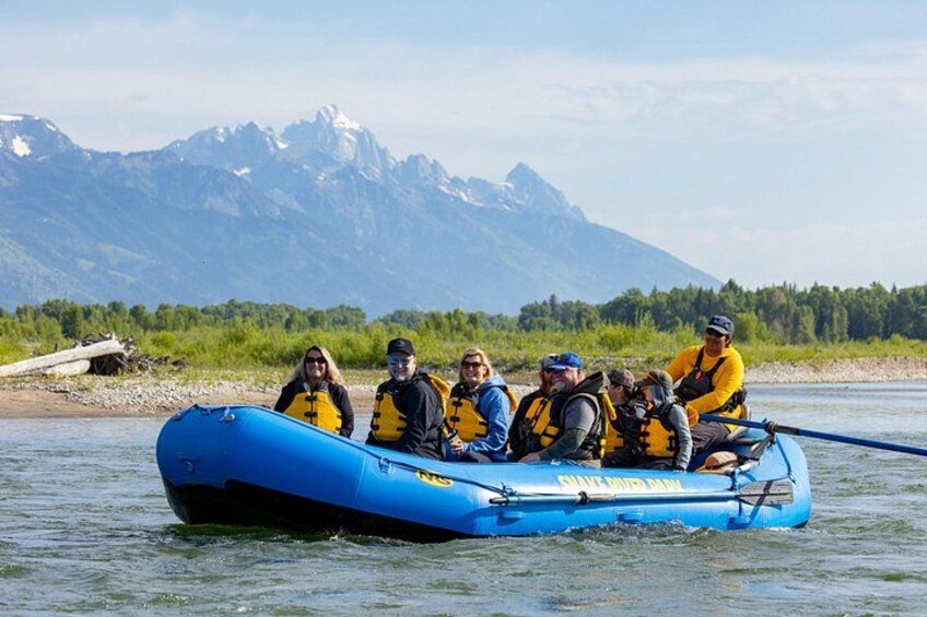 Un grupo de personas haciendo rafting en un bote inflable azul, con un paisaje montañoso al fondo. 2