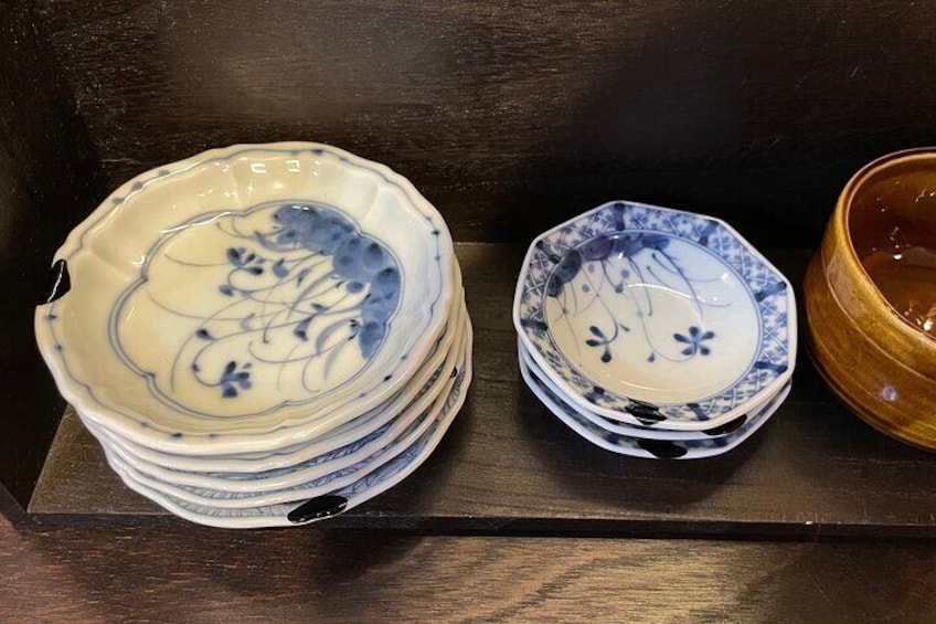 A stack of blue and white ceramic plates and bowls on a wooden shelf. 2