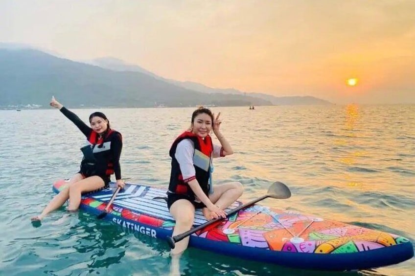 Two people on a colorful paddleboard in a body of water with a sunset in the background. 1