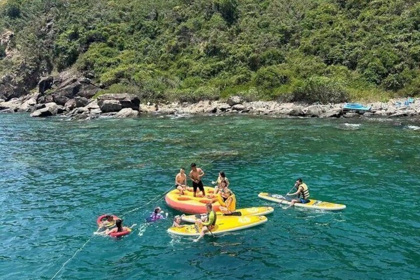 People on inflatable rafts in a clear blue sea with a rocky shoreline and greenery in the background. 3