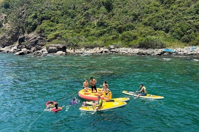 People on inflatable rafts in a body of water with a rocky shoreline and greenery in the background. 3