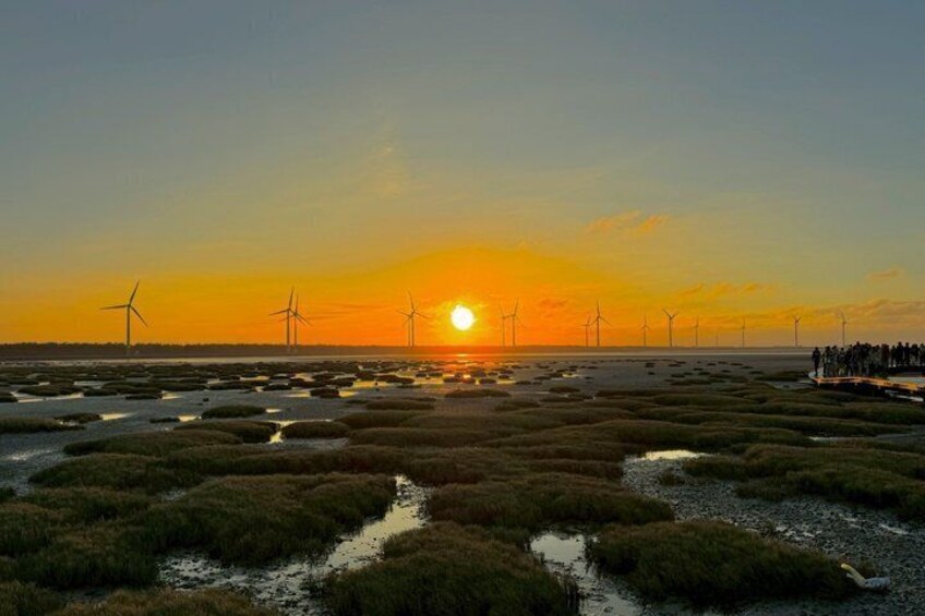 A sunset over a coastal landscape with wind turbines and a group of people on a boardwalk. 5
