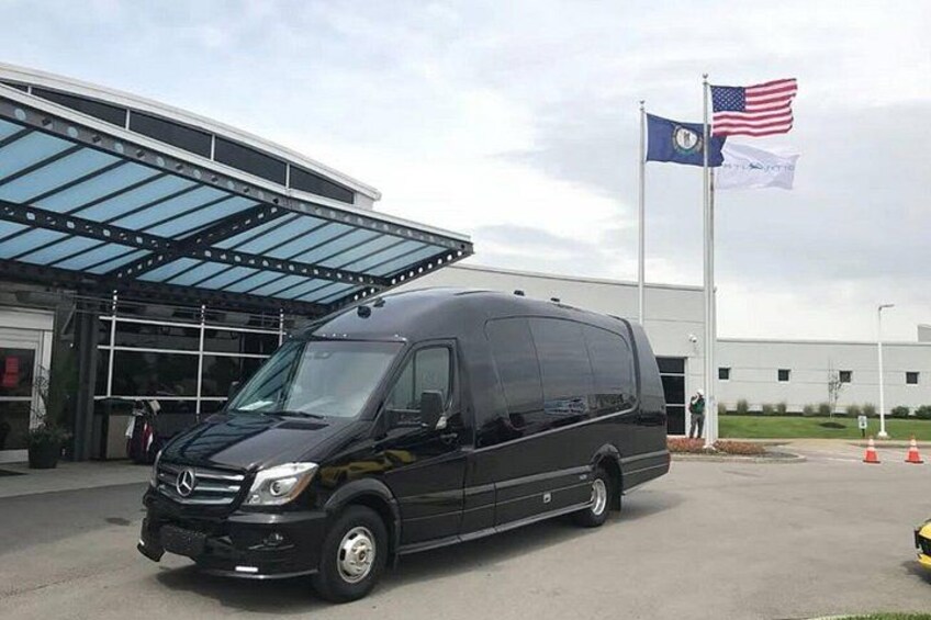 A black van parked in front of a building with a glass roof and two flags. 2