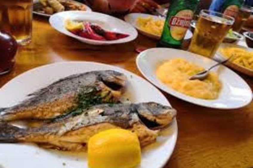 En tallerken med grillet fisk, et stykke citron og et glas øl på et bord. 5