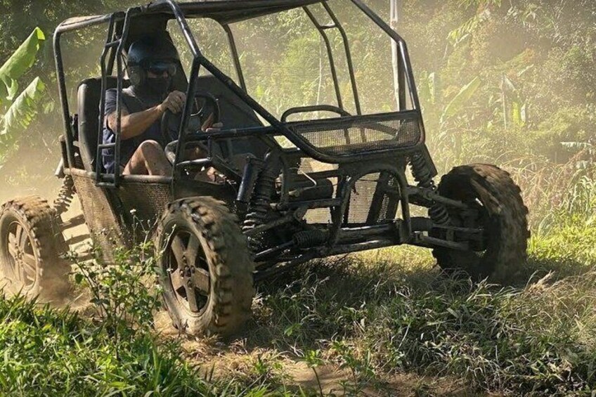 A person driving a four-wheeled off-road vehicle on a dirt path surrounded by greenery. 1