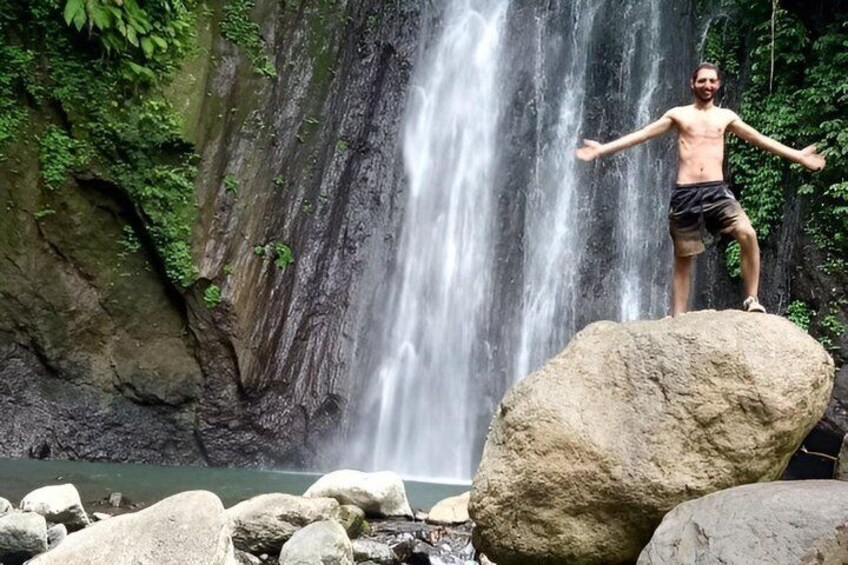 A person standing on a rock with arms outstretched in front of a waterfall. 2