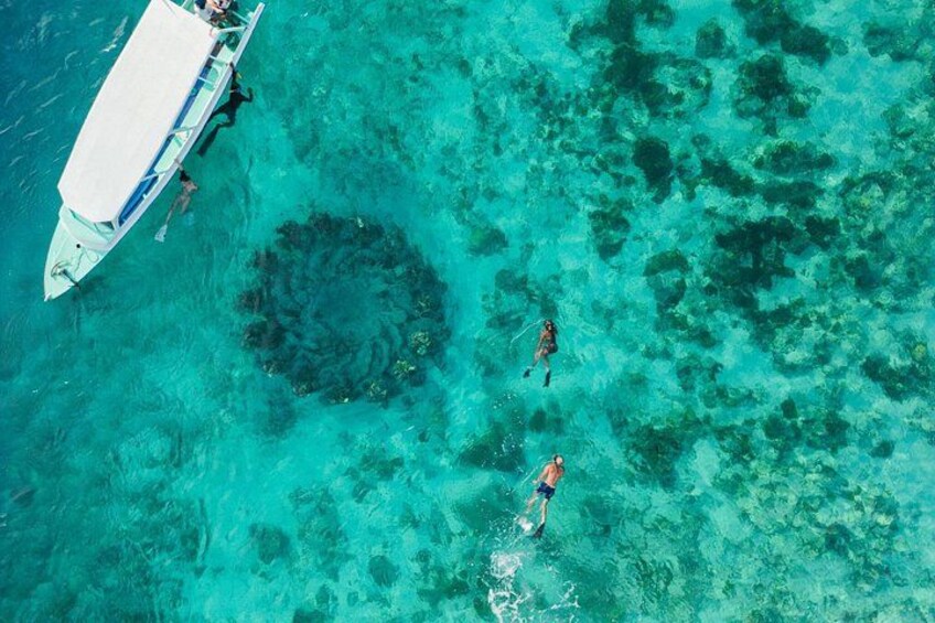 A boat anchored in clear turquoise waters with a person swimming nearby. 1