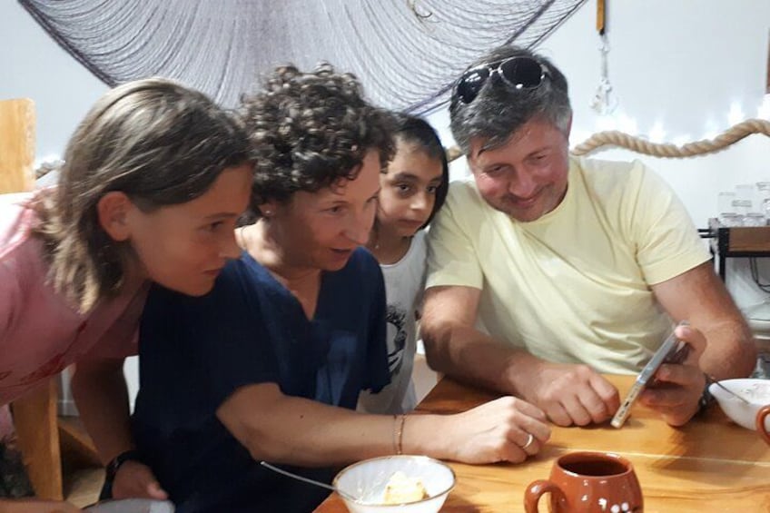 A group of people sitting around a wooden table with a rustic setting, including a rope and a hammock in the background. 2