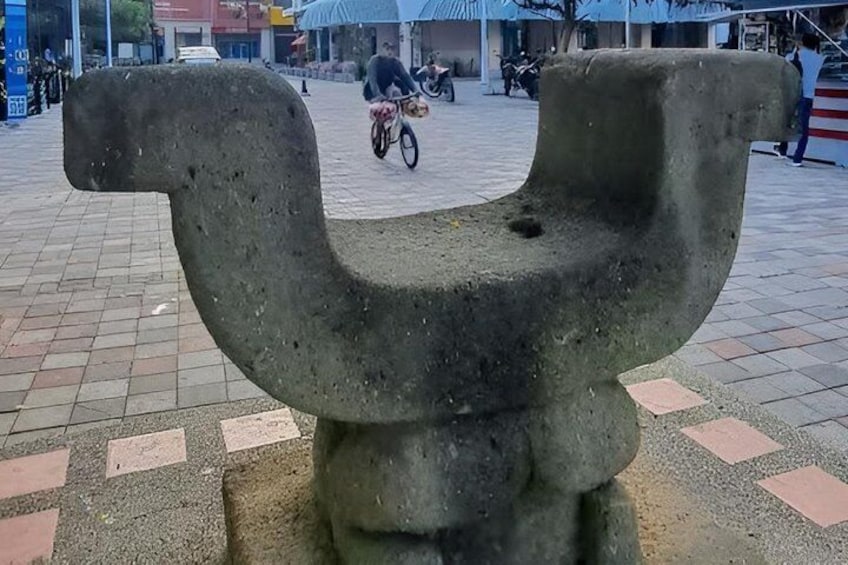 A large, abstract stone sculpture in an open plaza with a tiled ground. 3