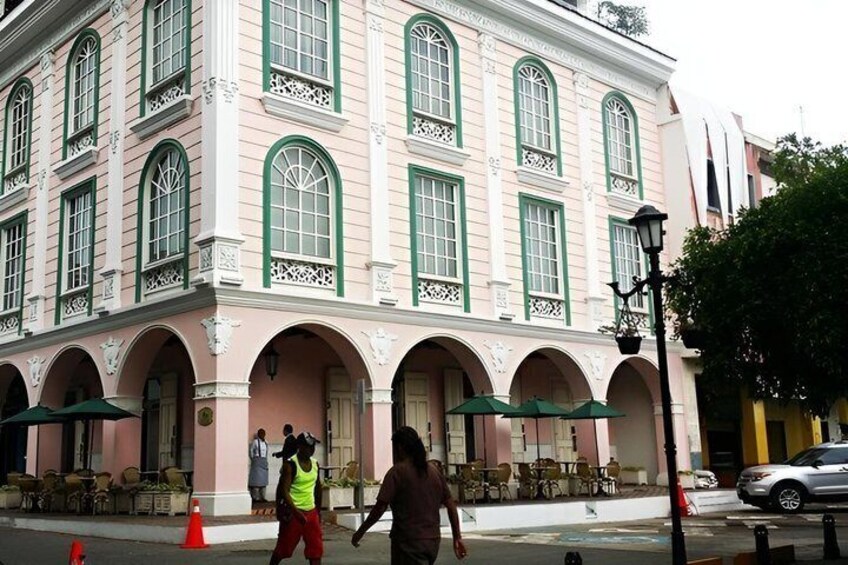 A pink building with green window frames and a covered outdoor seating area. 2