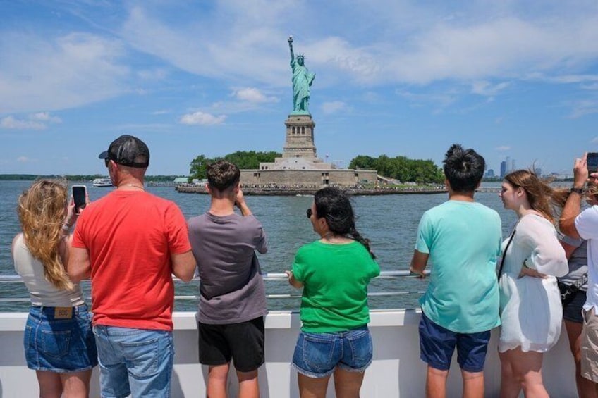 People standing by a waterfront, looking at the Statue of Liberty. 4