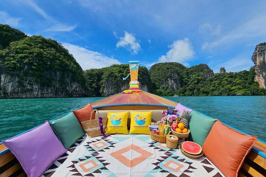 A boat with colorful cushions and a patterned mat, surrounded by clear turquoise water and green cliffs. 1