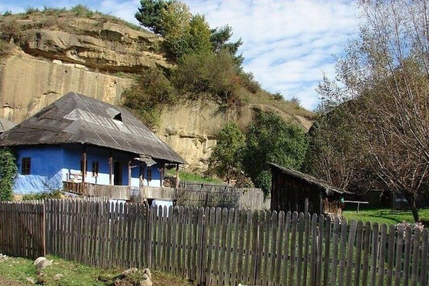 A rustic house with a blue exterior, a wooden fence, and a rocky hillside in the background. 4