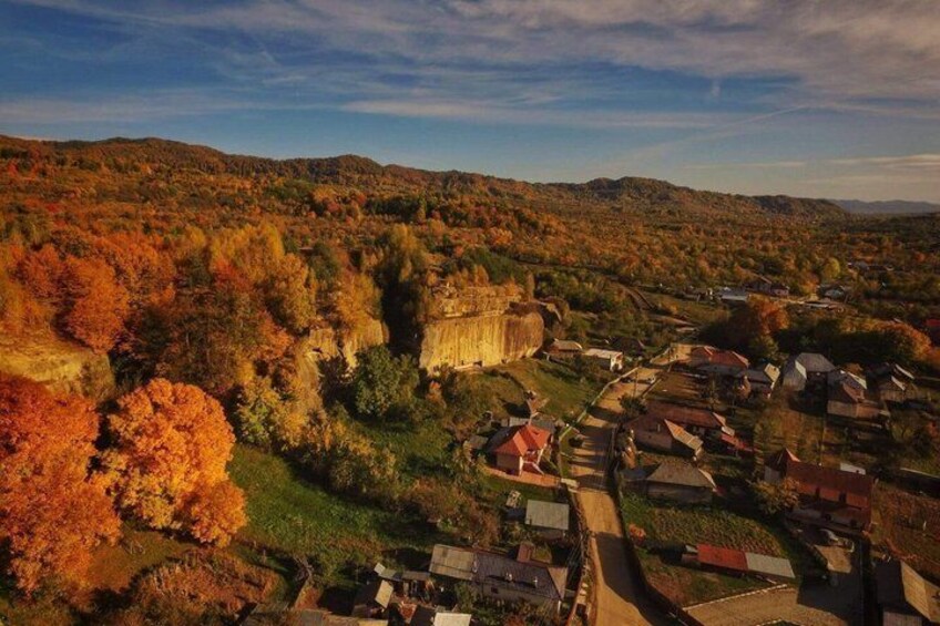 A town nestled in a valley with autumn foliage, surrounded by hills and a prominent castle-like structure. 1