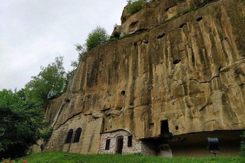A rock formation with multiple caves and a small building at its base. 5