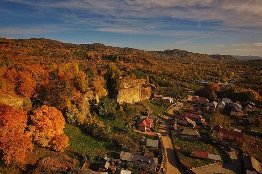 A town nestled in a valley with autumn foliage, surrounded by hills and a prominent stone structure. 1