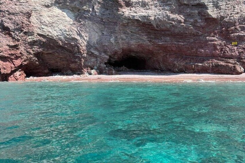 A coastal landscape with clear turquoise water, a rocky cliff, and a cave entrance. 3