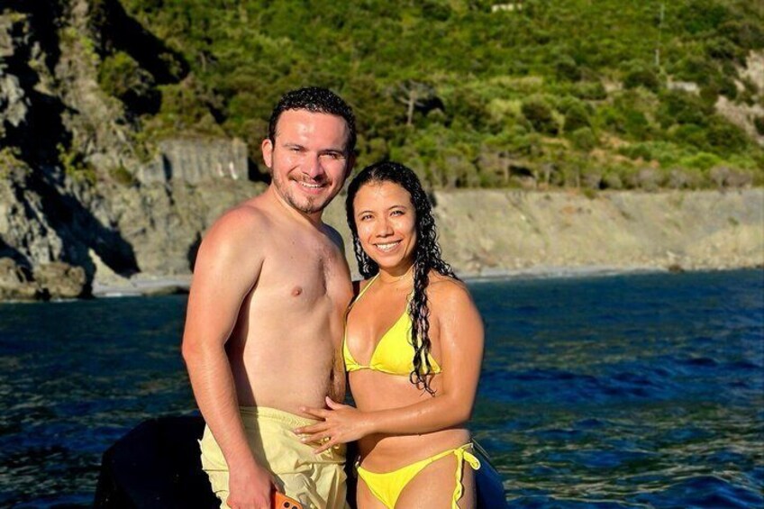 A couple standing by a rocky shoreline with clear blue water. 5