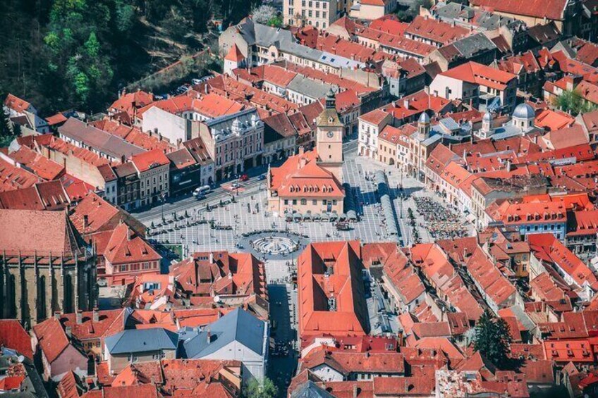 An aerial view of a town with red-roofed buildings, a central square, and a prominent clock tower. 2