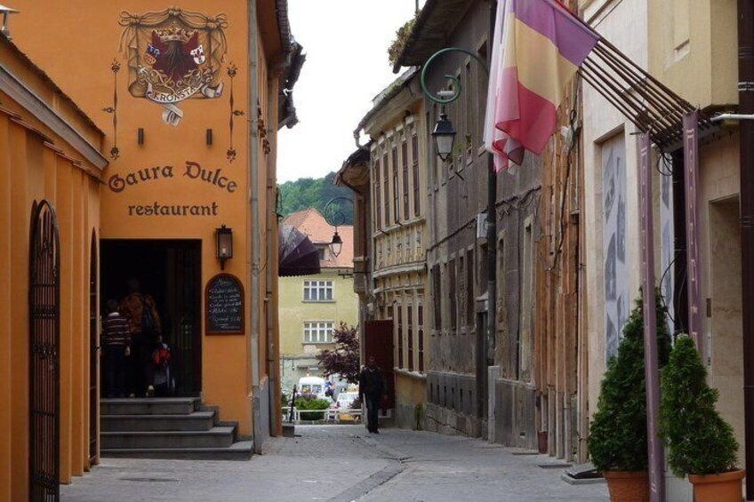 A narrow street with a restaurant named 'Gaura Dulce' on the left and a flag on the right. 4