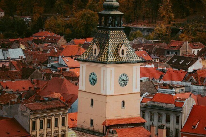 A clock tower with a green and yellow patterned roof, surrounded by red-roofed buildings. 3