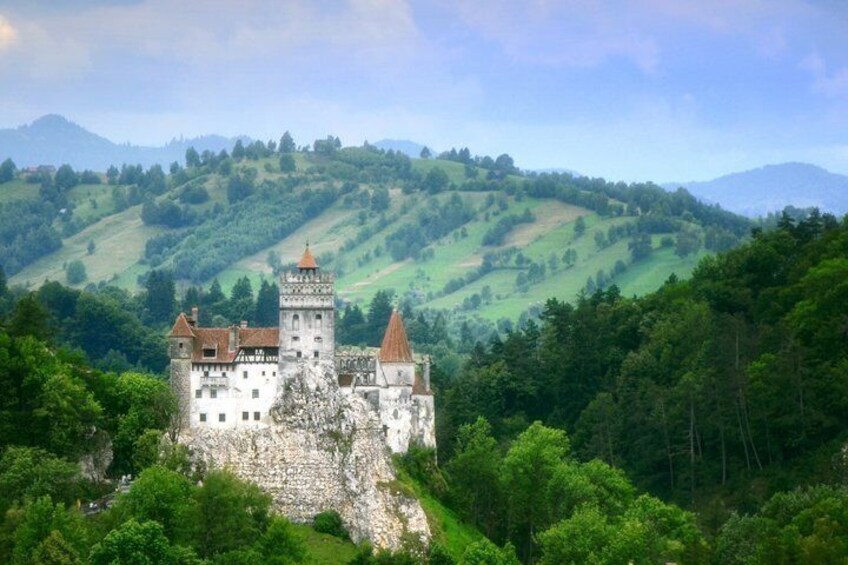 A historic castle on a hill with surrounding greenery and hills in the background. 1