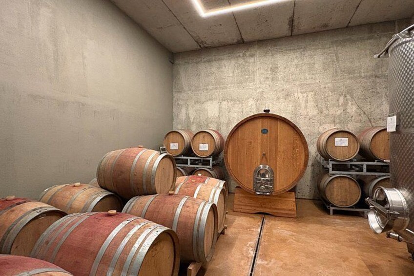 Wooden wine barrels stacked in a cellar with a concrete floor and walls. 5