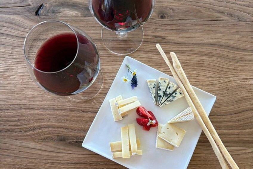 A wooden table with a white plate of cheese, strawberries, and a glass of red wine. 3