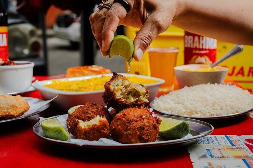 A hand holding a lime slice over a plate of food, with various dishes in the background. 2