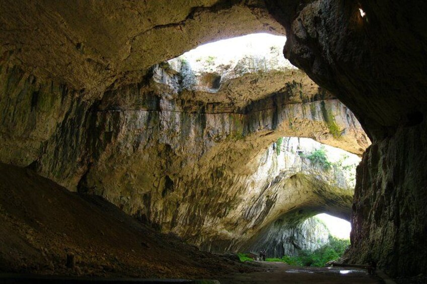 A cave with a natural archway and a stream running through it. 3