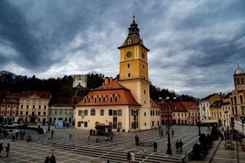 A historic square with a prominent clock tower, surrounded by traditional buildings and a large open space. 1